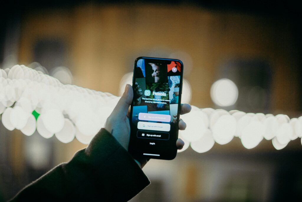 A hand holding a smartphone displaying an app login screen with a vibrant bokeh light background.